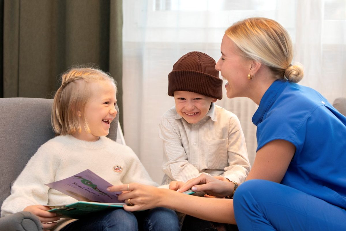 Zahnärztin Dr. Lisa-Maria Bechter lacht beim Vorlesen mit zwei Kindern im Empfangsbereich